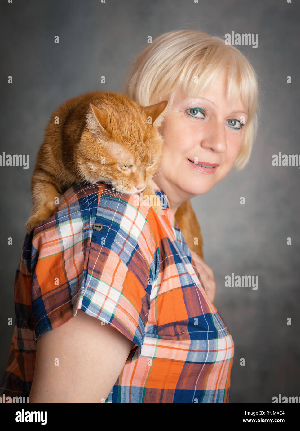 Schön gealterte Frau umarmte ihre rote Katze auf grauem Hintergrund. Fokus auf eine Katze Stockfoto