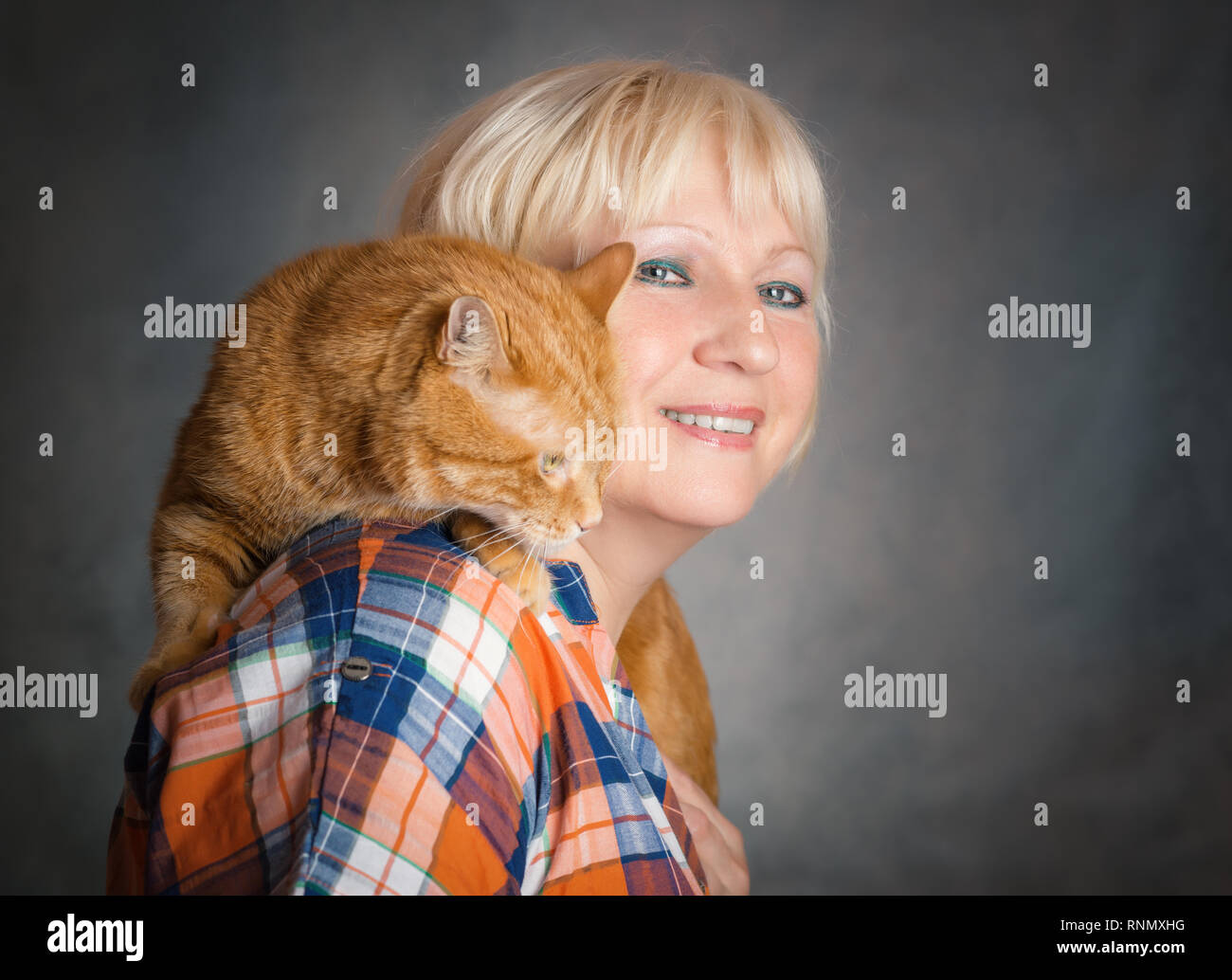Schön gealterte Frau umarmte ihre rote Katze auf grauem Hintergrund. Stockfoto
