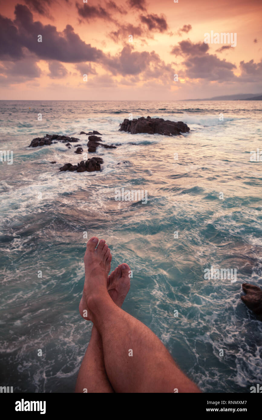 Vertikale Sommer coastal Marine bei Sonnenuntergang mit Beinen von entspannenden Mann am Strand Stockfoto