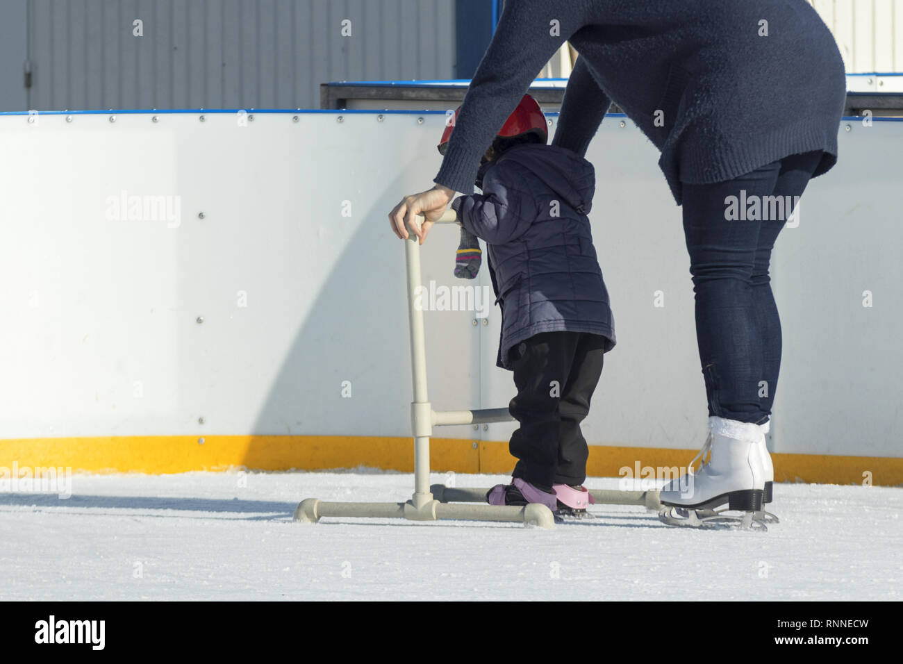 Kleines Kind erfahren Sie, wie Sie auf der Eisbahn mit Hilfe von Erwachsenen zu skaten. Ein kleines Kind und Erwachsener famale Supervisor sind, die die Förderung skate Struct Stockfoto