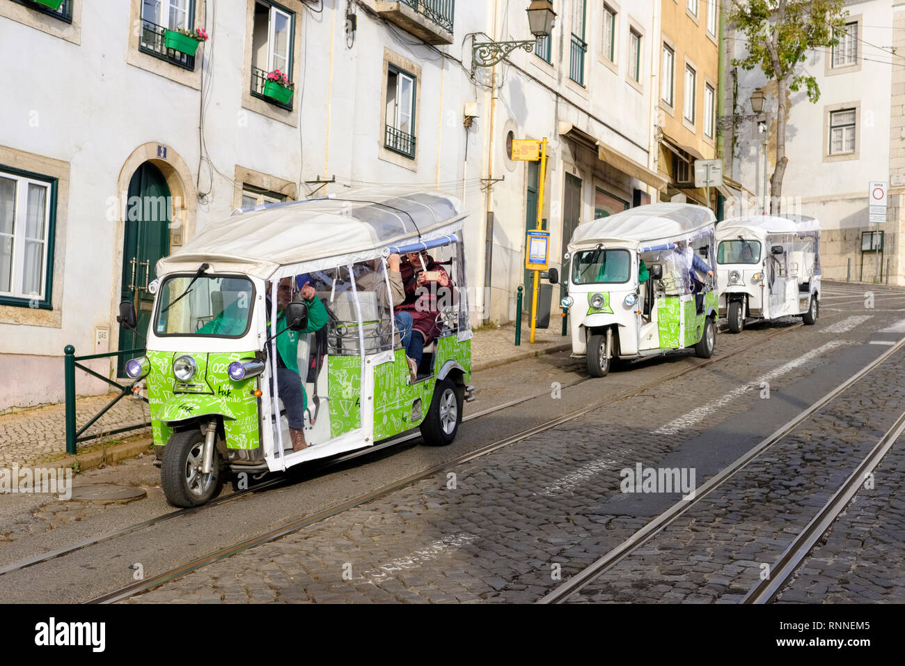 Touristen, die in Lissabon eine City Tour in elektrischen Tuk Tuk nehmen. Largo São Martinho, Lisboa, Portugal. Stockfoto