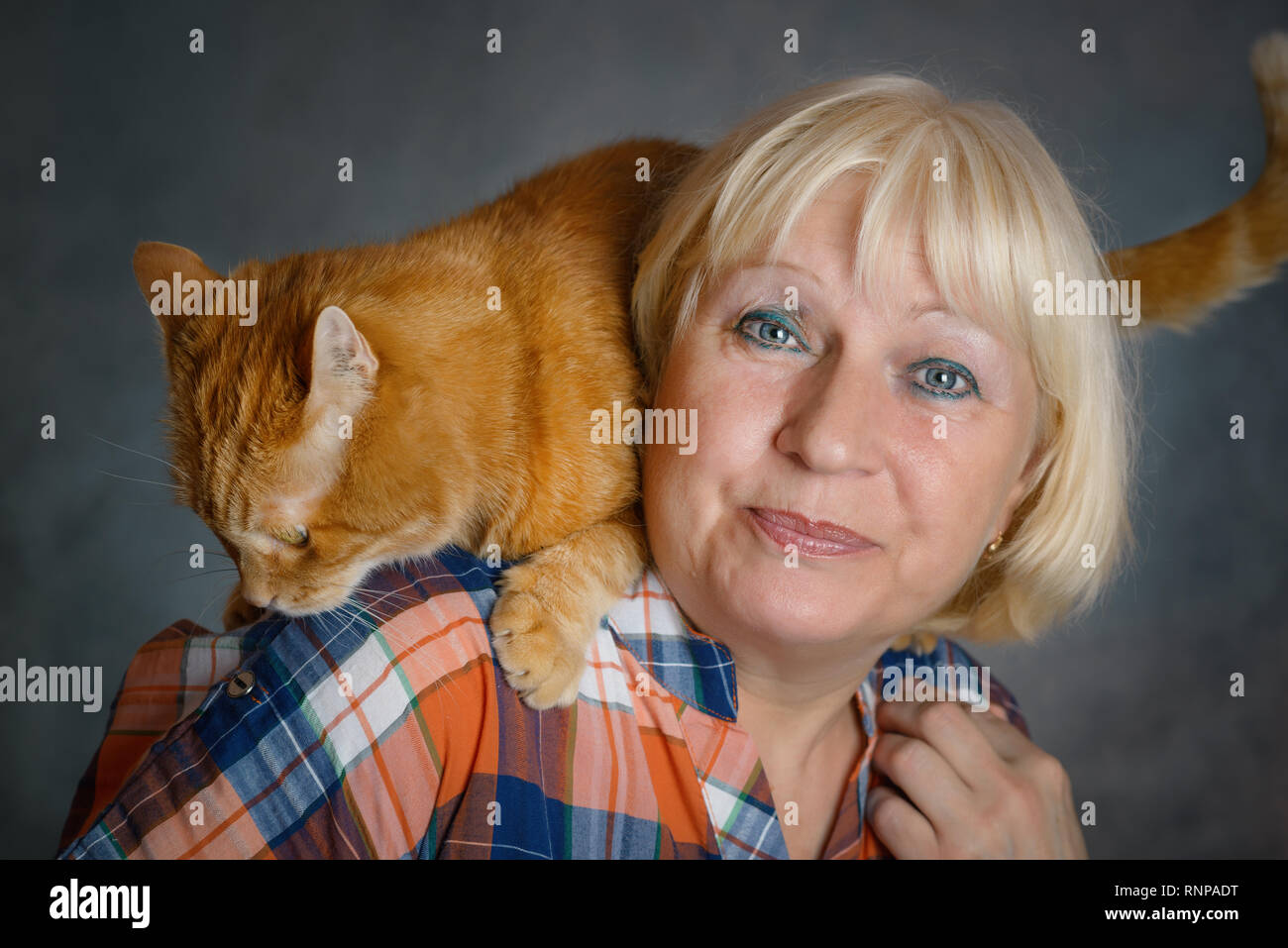 Schön gealterte Frau umarmte ihre rote Katze auf grauem Hintergrund. Stockfoto