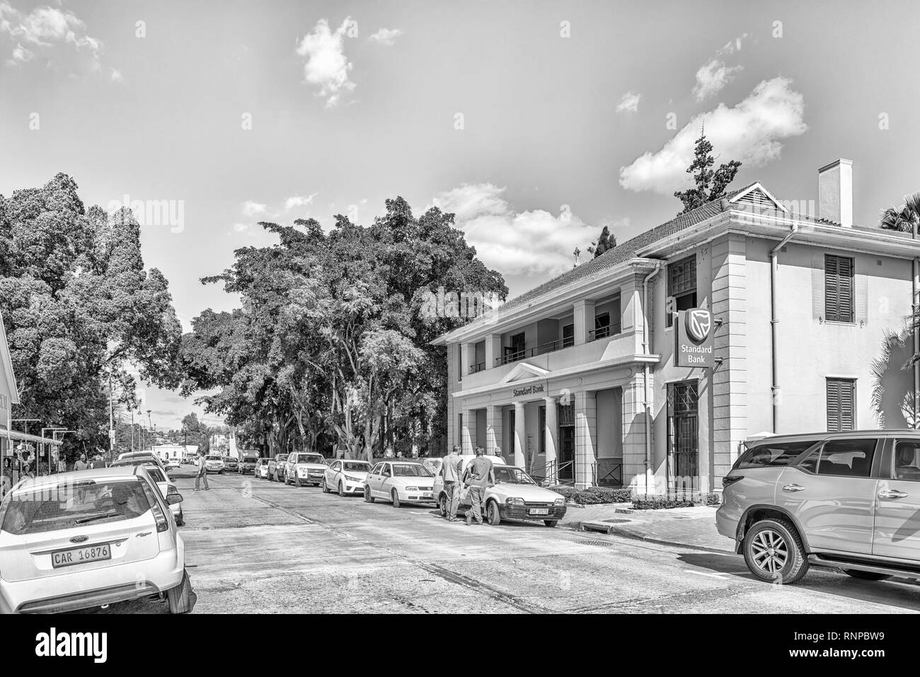 CLANWILLIAM, SÜDAFRIKA, 22. AUGUST 2018: eine Straße, Szene, mit einer Bank, Personen und Fahrzeuge, in Clanwilliam in der Western Cape Provinz. Schwarzweiß Stockfoto