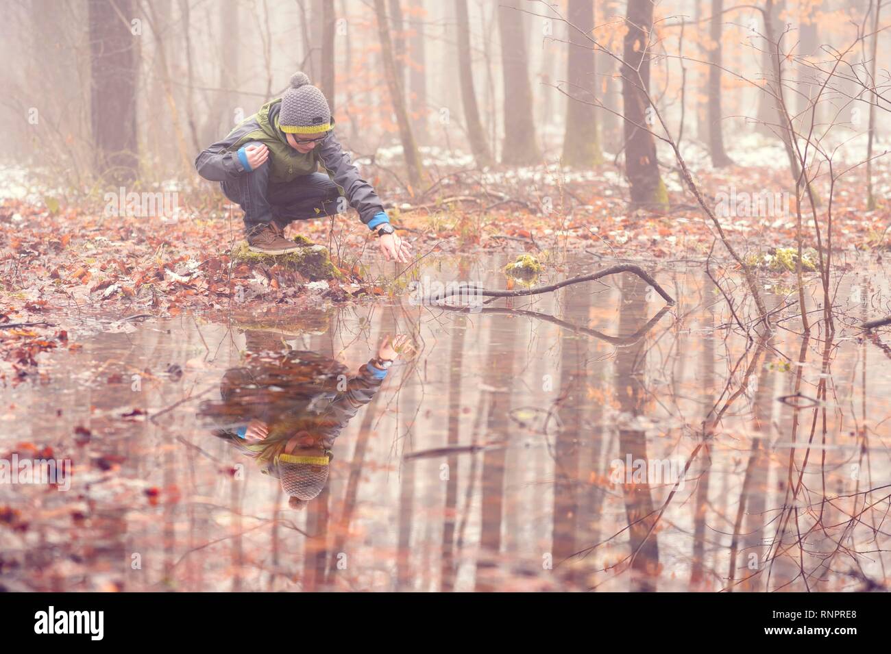 Junge, 10 Jahre, in den Wald im Nebel, spielen bei Pfütze, Spiegelung, Baden Württemberg, Deutschland Stockfoto