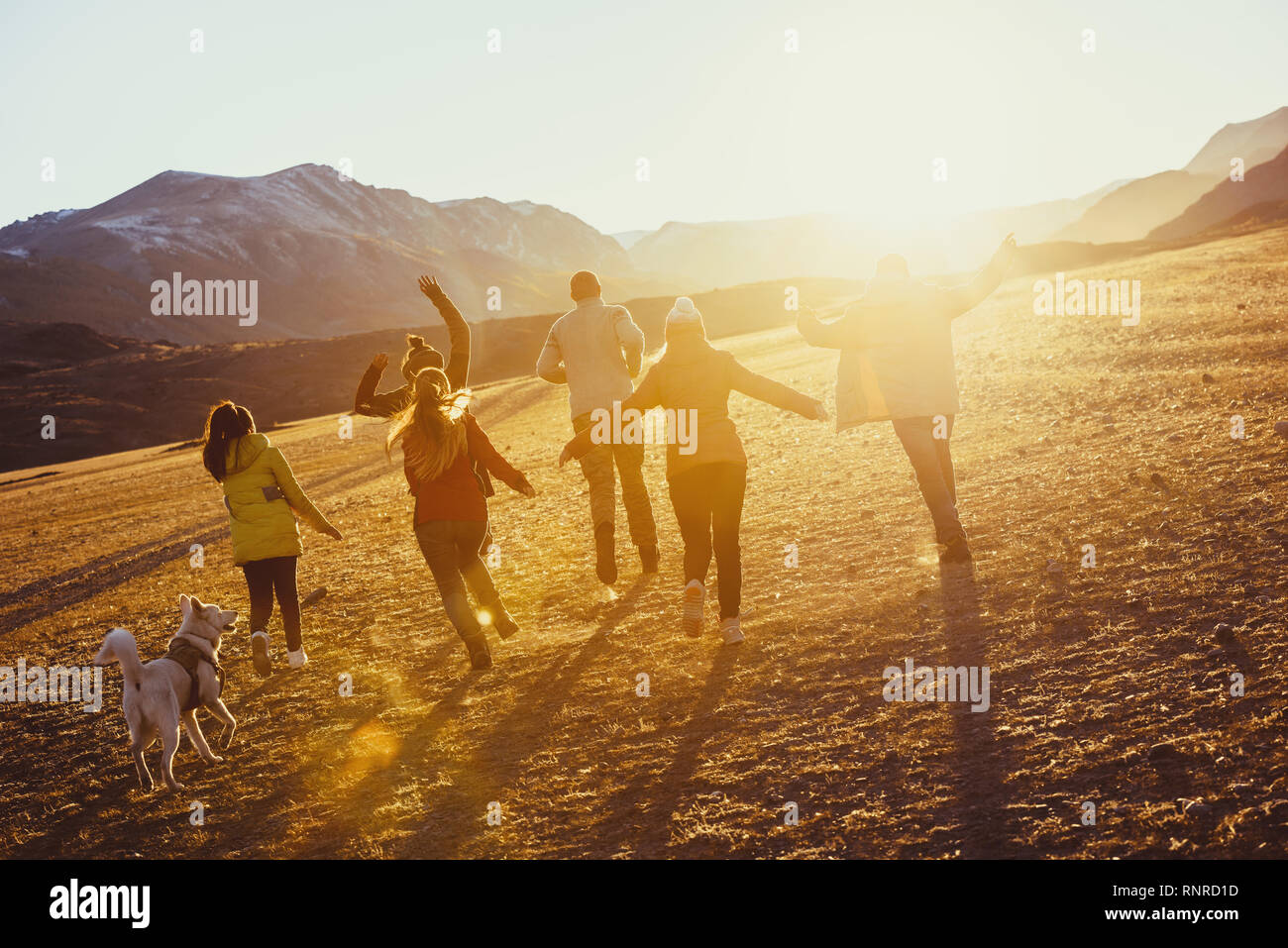 Große Gruppe der glückliche Freunde laufen und springen bei Sonnenuntergang Feld gegen Berge und Sonne Stockfoto