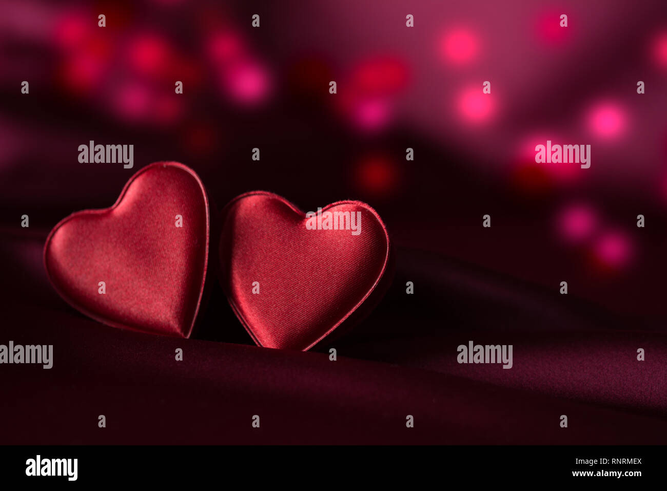 Zwei rote Herzen auf lila satin mit feinen roten und violetten Bokeh im Hintergrund Stockfoto