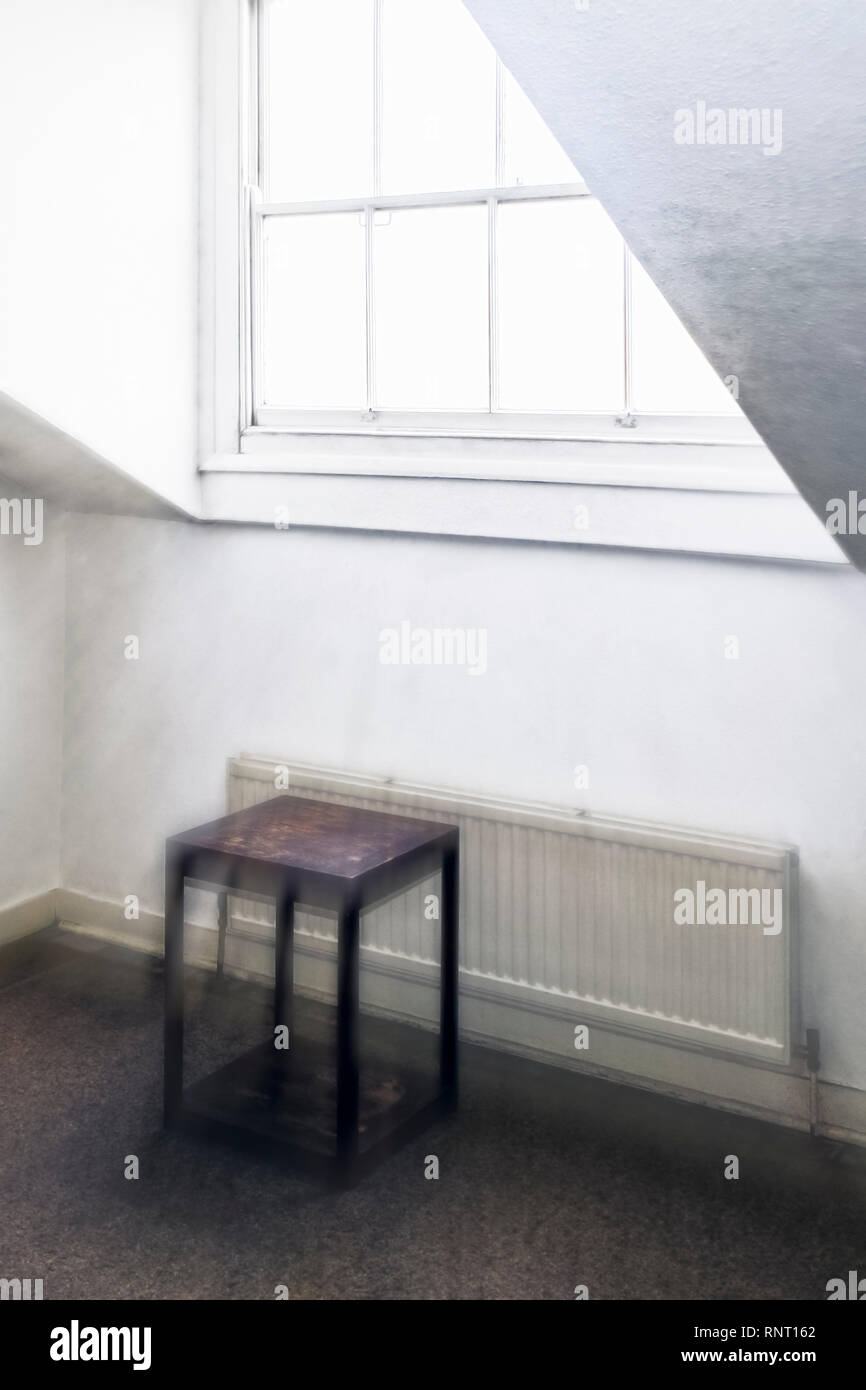 Geisterhafte zoom verschwommenes Bild von einem hell beleuchteten Schiebefenster in einer trostlosen Zimmer im Dachgeschoss eines alten Hauses, mit einem kleinen Holztisch und Kühler Stockfoto