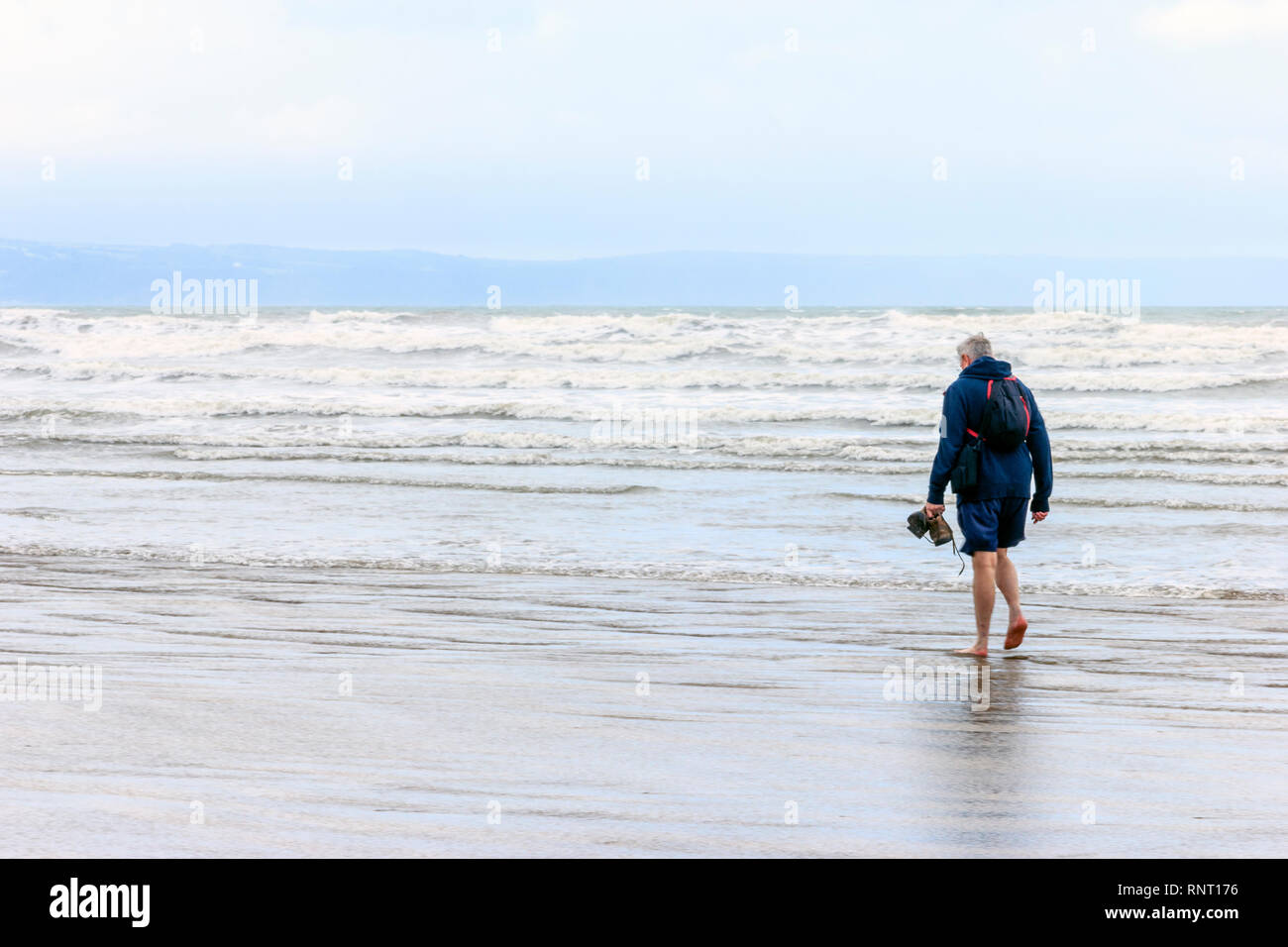 Single mann Barfuß im seichten Wasser am Strand von Westward Ho!, Devon, Großbritannien, an einem verregneten und nebligen Sommer morgen Stockfoto