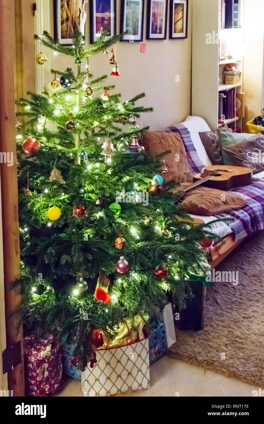 Aufgewickelte Weihnachtsgeschenke durch eine traditionelle Baum mit Lichtern und Kugeln in eine Familie zu Hause, London, UK Stockfoto