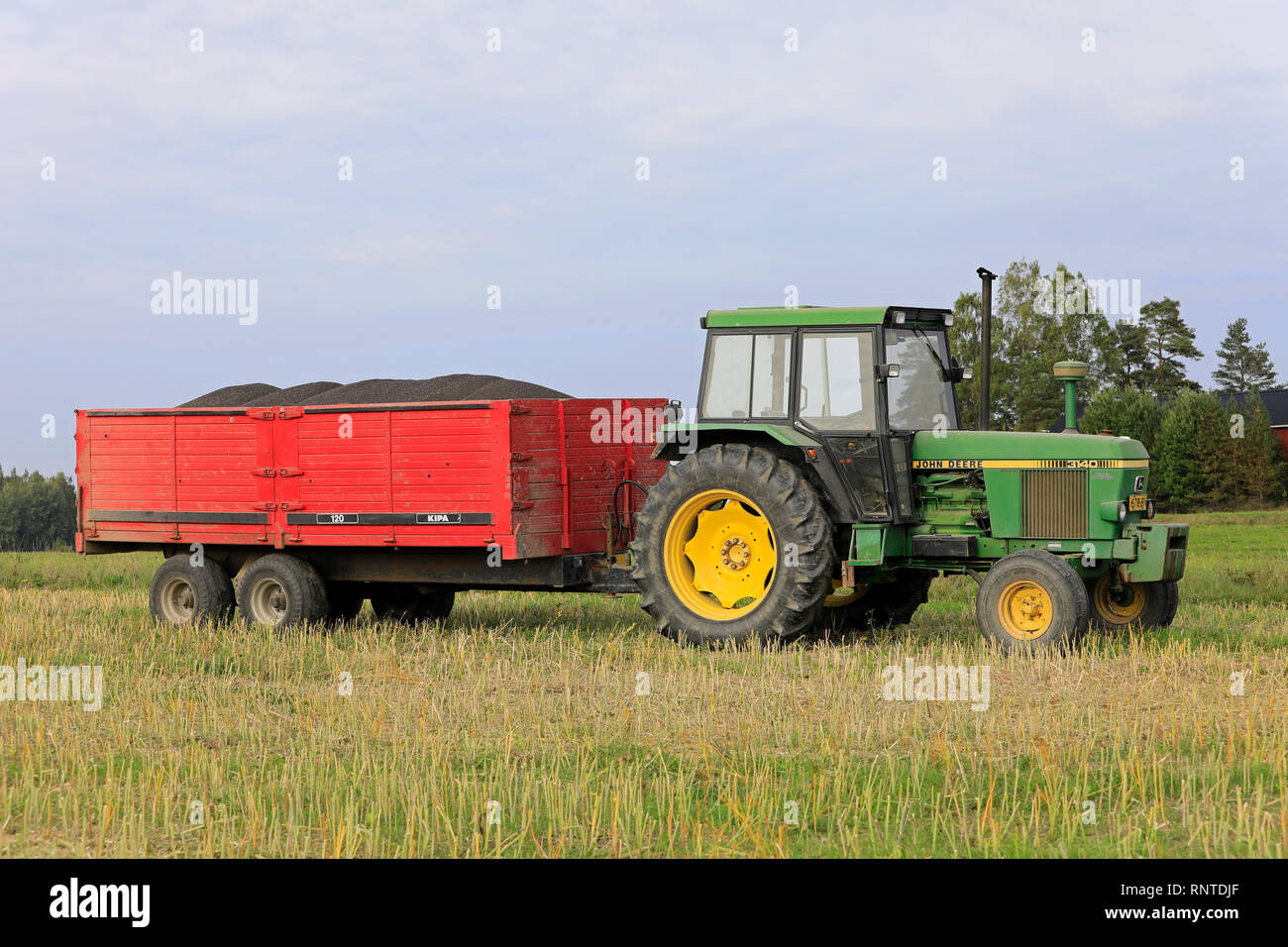 Salo, Finnland - 8 September, 2018: John Deere 3140 farm Traktor im Feld vor der landwirtschaftlichen Anhänger mit Ladung der geernteten Raps im Herbst. Stockfoto