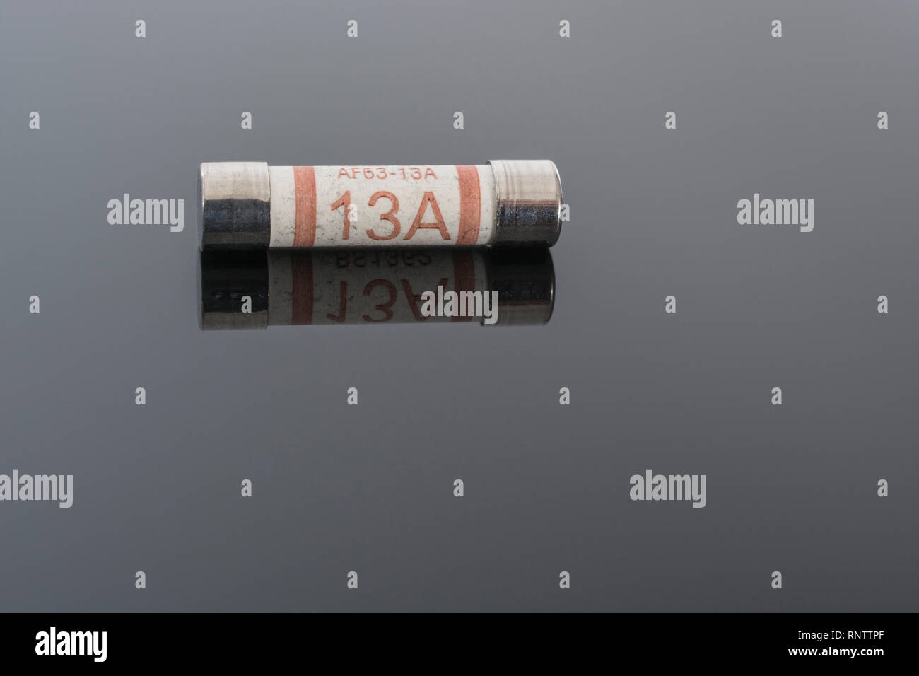 Haushaltsgeräte elektrische 13-A-Sicherung (Keramik- Kartusche Art) auf reflektierenden schwarzen Hintergrund. Metapher die elektrische Sicherheit. 25 mm L x 6,3 D Stockfoto
