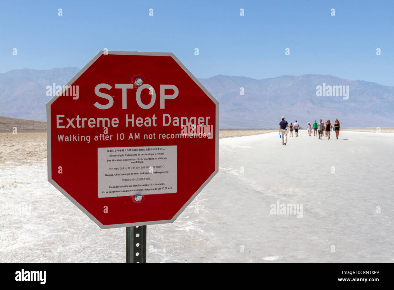 Ein TOP Extreme Hitze Gefahr' Schild gesehen, wie Menschen gehen auf Badwater Basin, Death Valley National Park, California, United States. Stockfoto