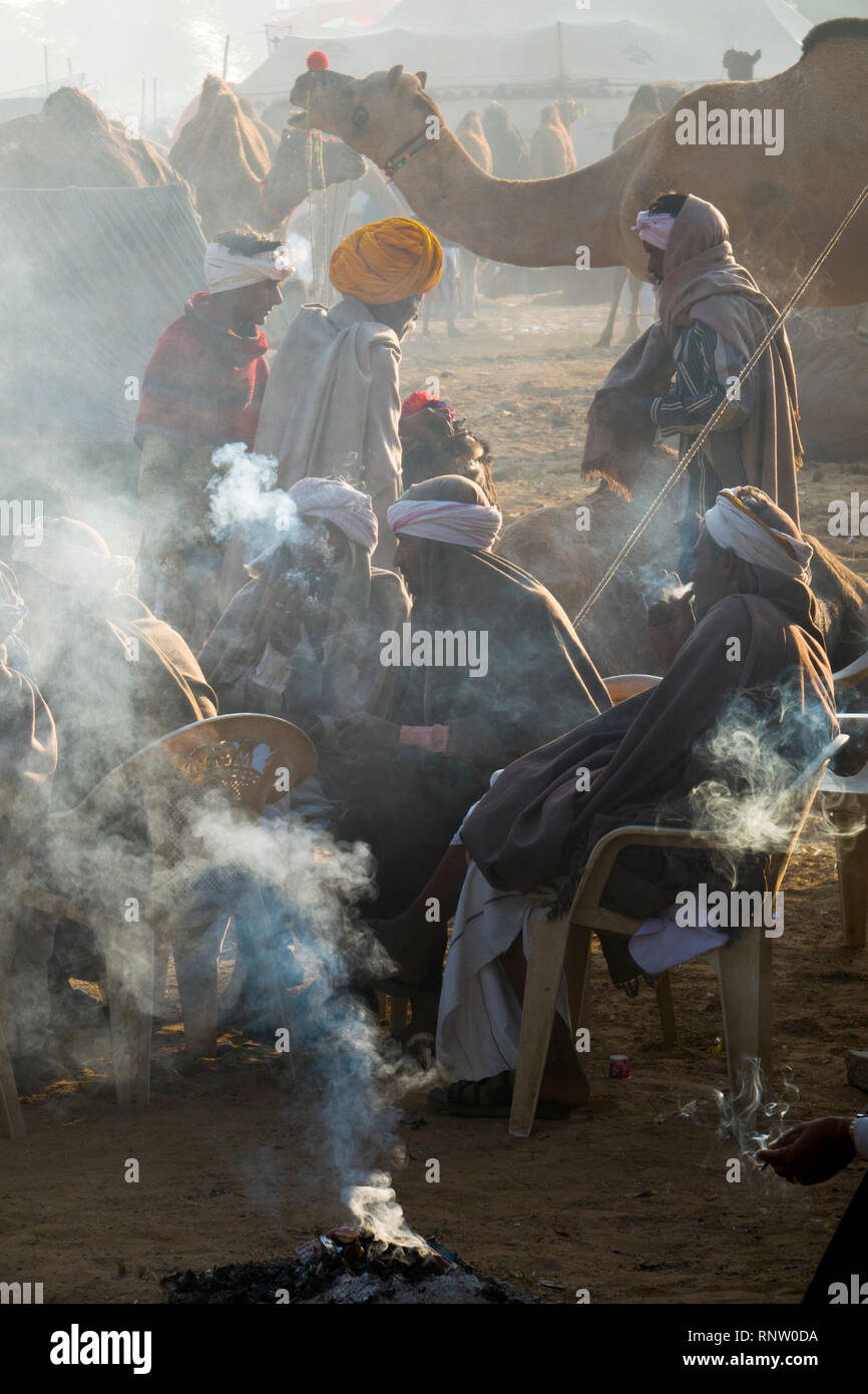 Raika Kamelhirten sitzen Rauchen um ein rauchiges Feuer, während ein kalter Wintermorgen am Pushkar Camel Fair in Rajasthan, Indien Stockfoto