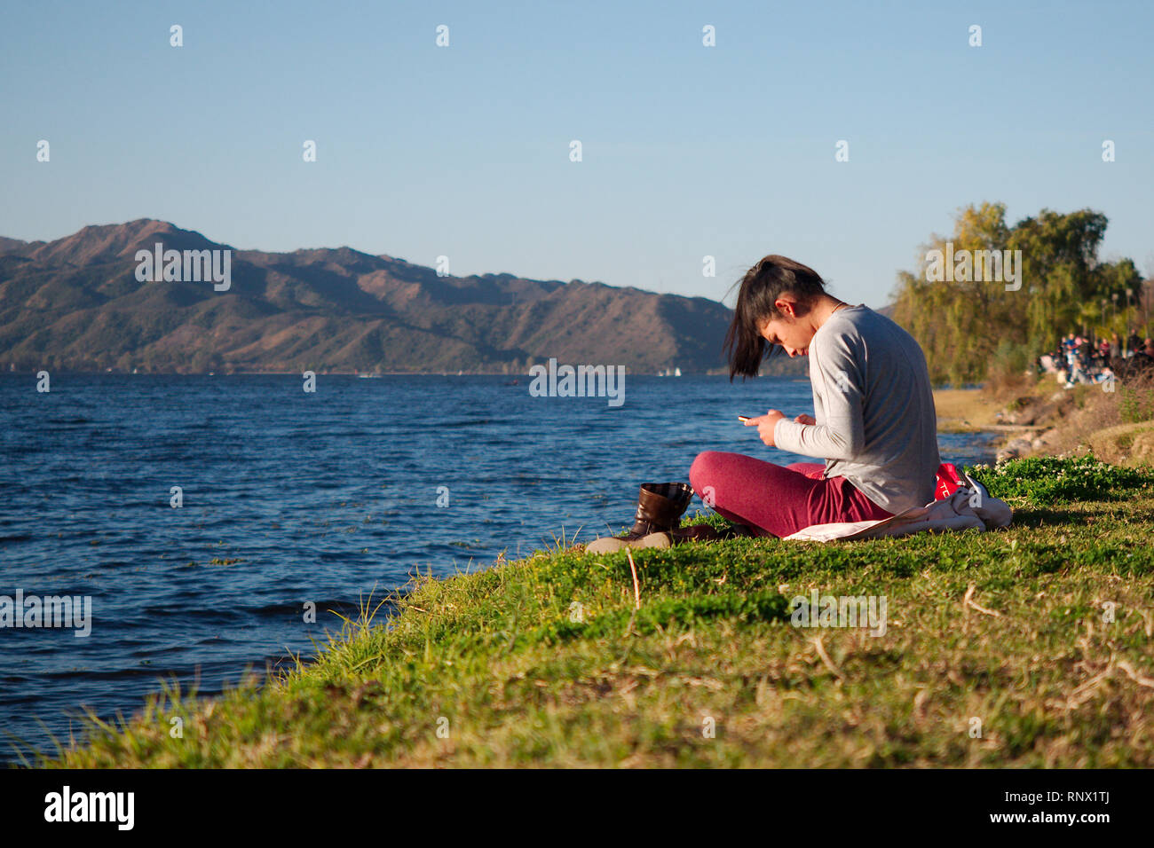 Villa Carlos Paz, Cordoba, Argentinien - 2019: Eine junge Frau liegt mit ihren Schuhen durch die San Roque See an einem Sonntag Abend. Stockfoto