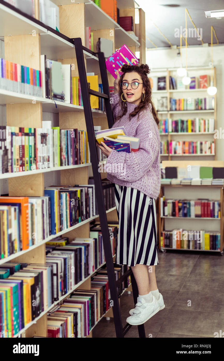 Positive junge Dame im weißen Turnschuhen lehnte sich auf schwarze Treppe Stockfoto