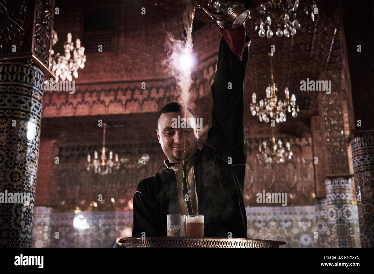 Ein Kellner gießt dampfend heißen süßen Pfefferminztee aus großer Höhe in einem beliebten Restaurant in Marrakesch, Marokko sporting mosaic Säulen und Kronleuchtern. Stockfoto