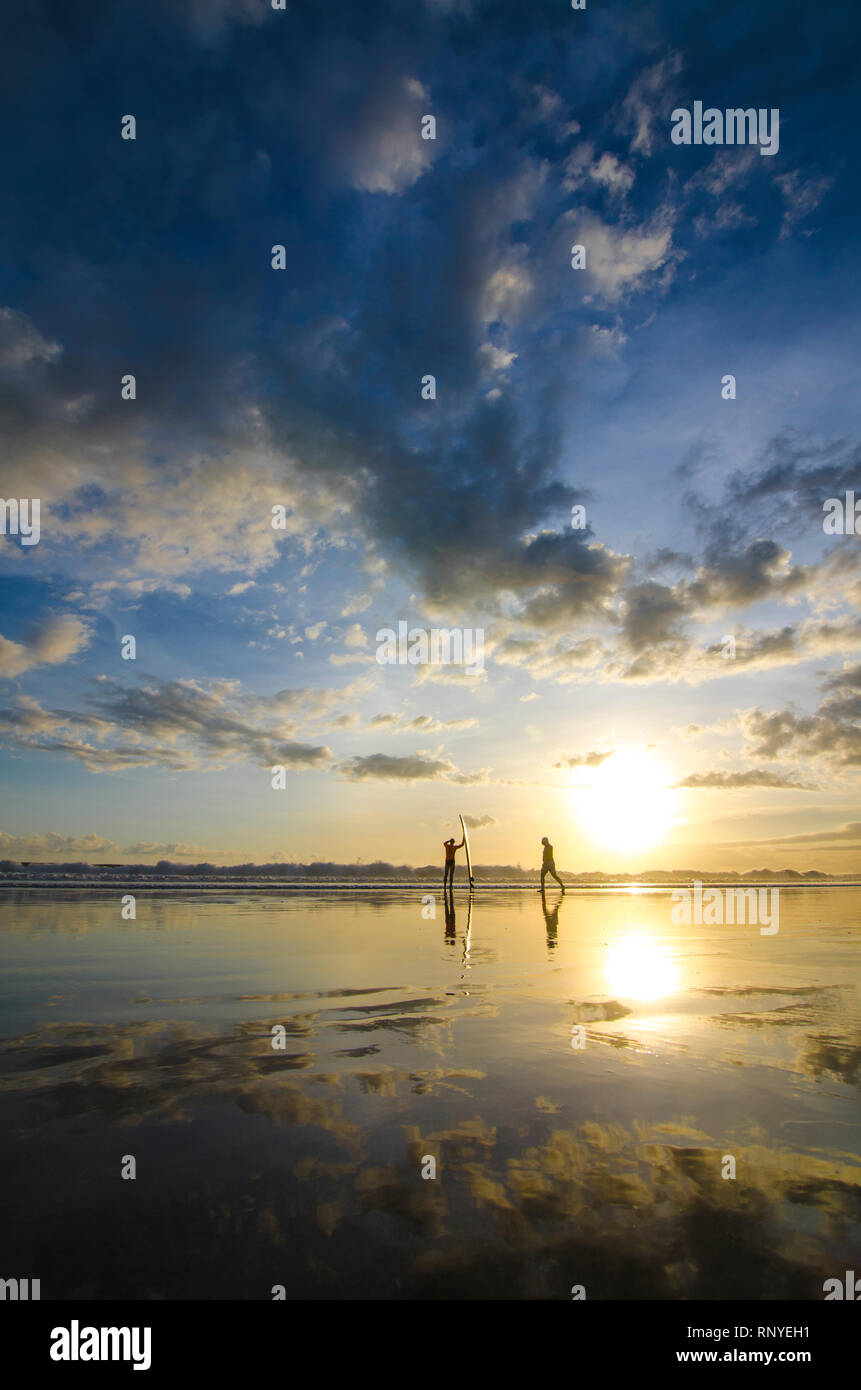 Zwei Kerle haben eine Übung am Ufer mit Surfbrett beim Sonnenuntergang am Strand von Double Six, Legian, Seminyak, Kuta, Bali, Indonesien Stockfoto