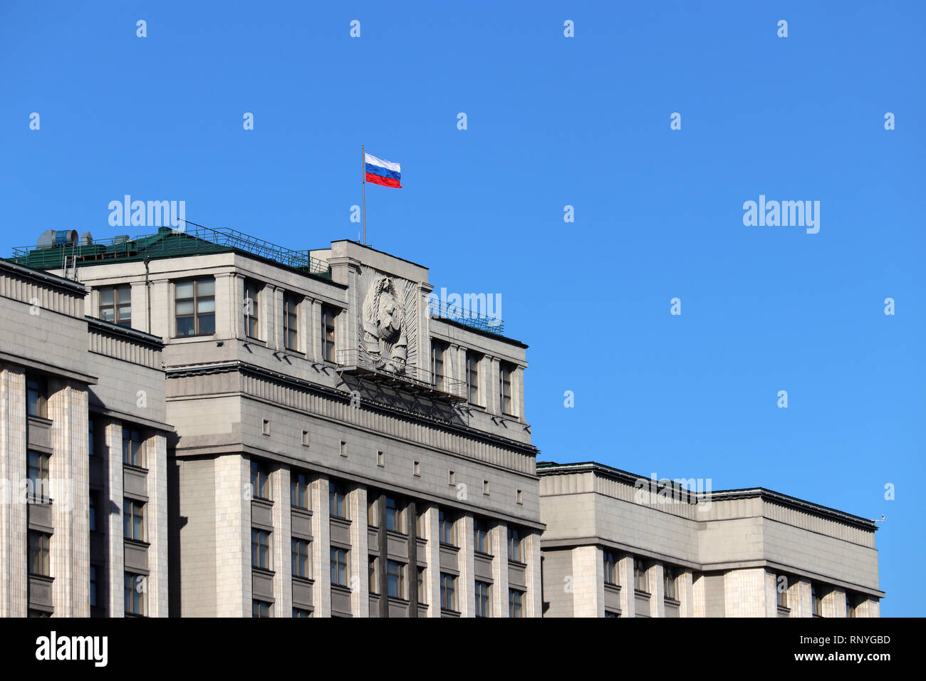 Russische Flagge auf dem Parlamentsgebäude in Moskau gegen den blauen Himmel. Fassade der Staatsduma Russlands mit sowjetischen Wappen, russischen Behörde Stockfoto
