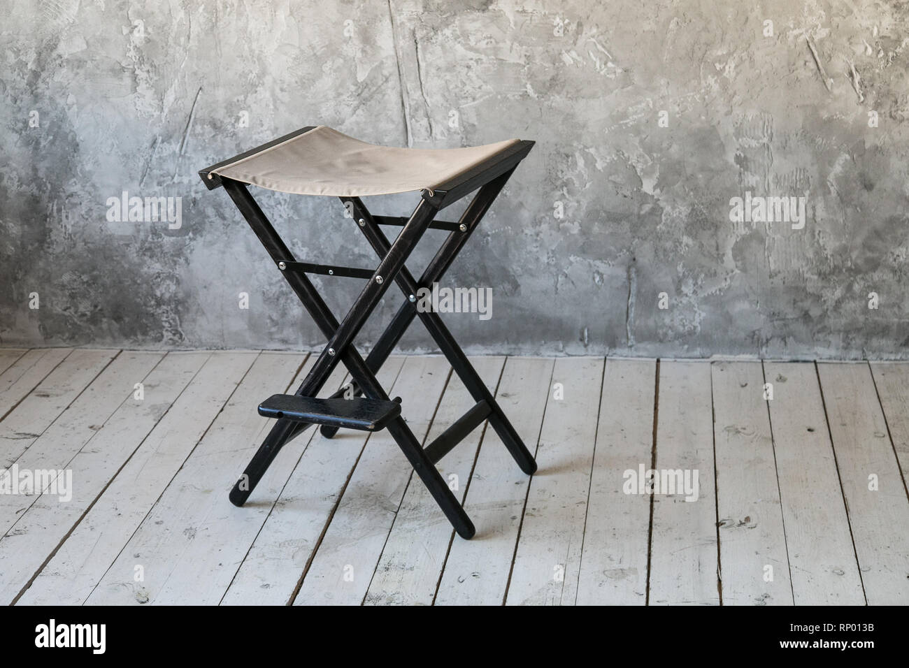 Director's Chair auf Beton Wand Hintergrund. Loft Zimmer. Holzboden. Tageslicht. Freier Platz für Text. Stockfoto