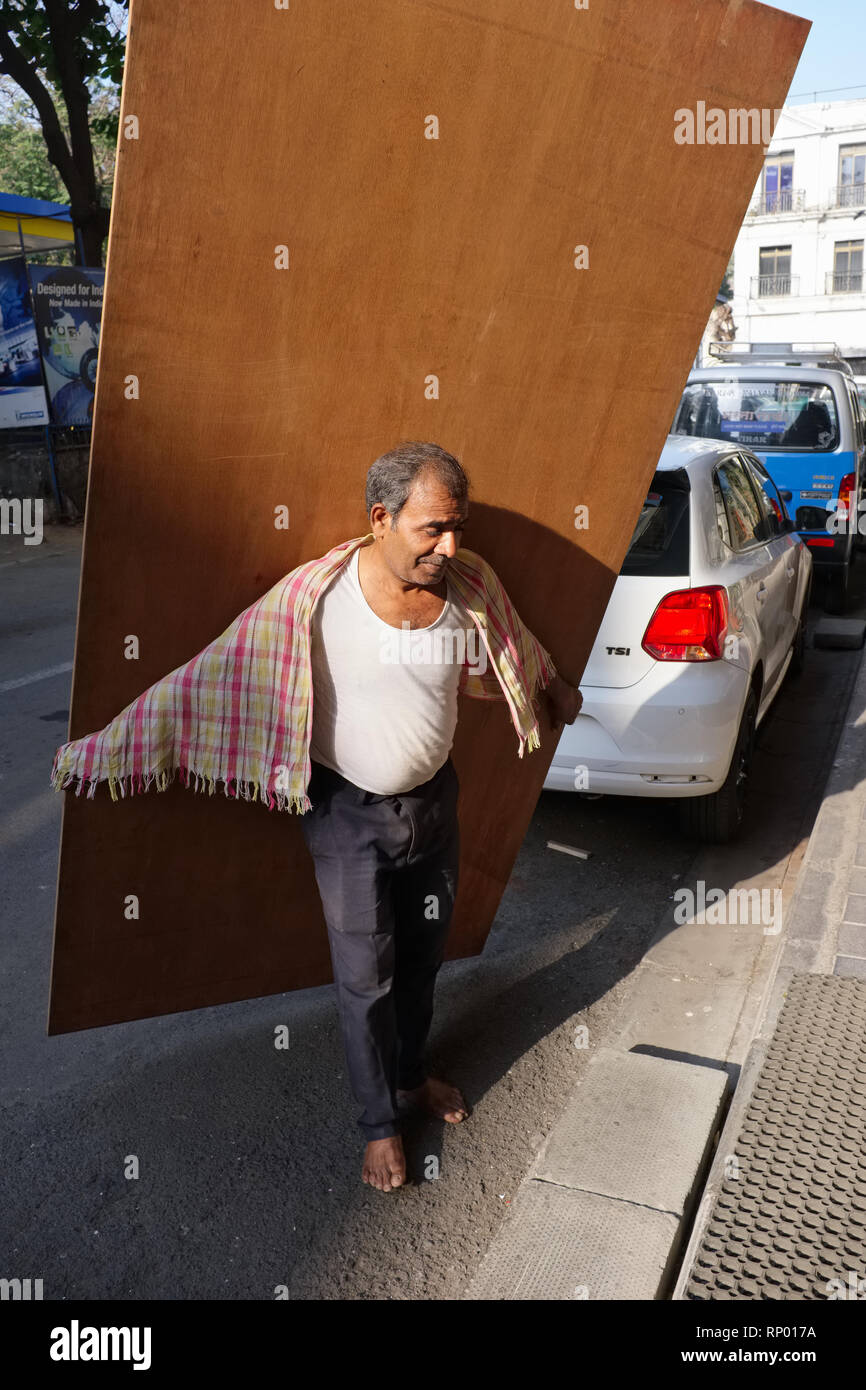 Eine barfuß Tischler in Mumbai, Indien, über ein Holzbrett, schätzungsweise 50 Kilo, mehrere Etagen in einem Gebäude wiegen zu tragen Stockfoto