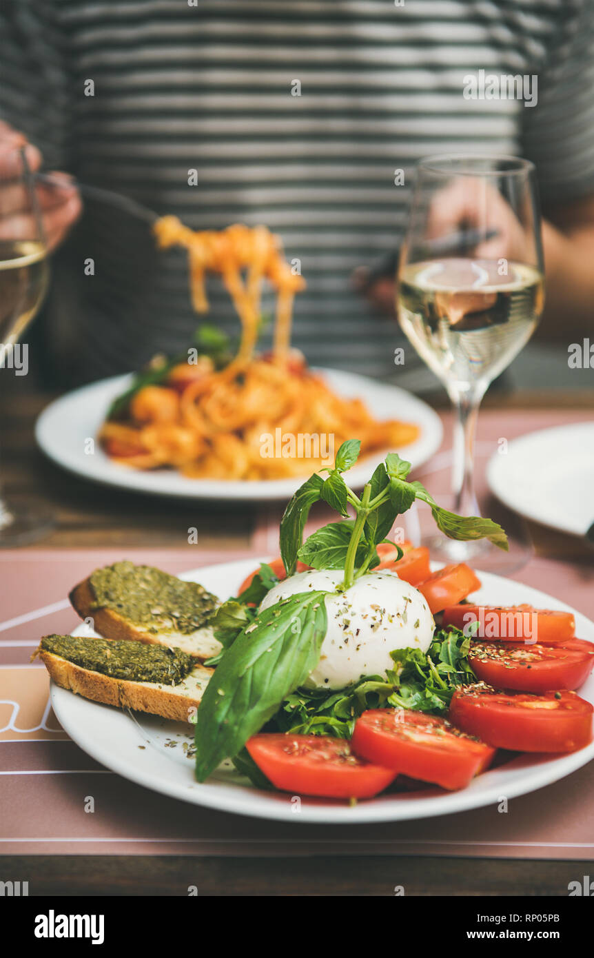 Italienisches Abendessen im Bistrot mit Caprese Salat mit Mozzarella, Tomaten, Basilikum, Toast, Spaghetti Pesto Pasta, Weißwein. Mann essen Pasta, in suchen Stockfoto