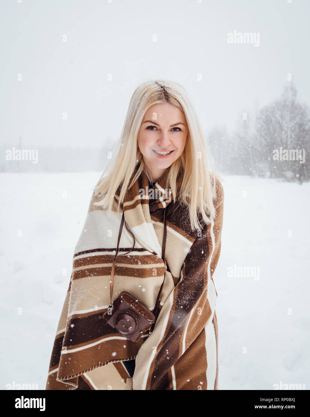 Schöne blonde Mädchen mit einem Vintage Kamera lächelnd vor dem Hintergrund einer Winterlandschaft. Nikola-Lenivets, Russland Stockfoto