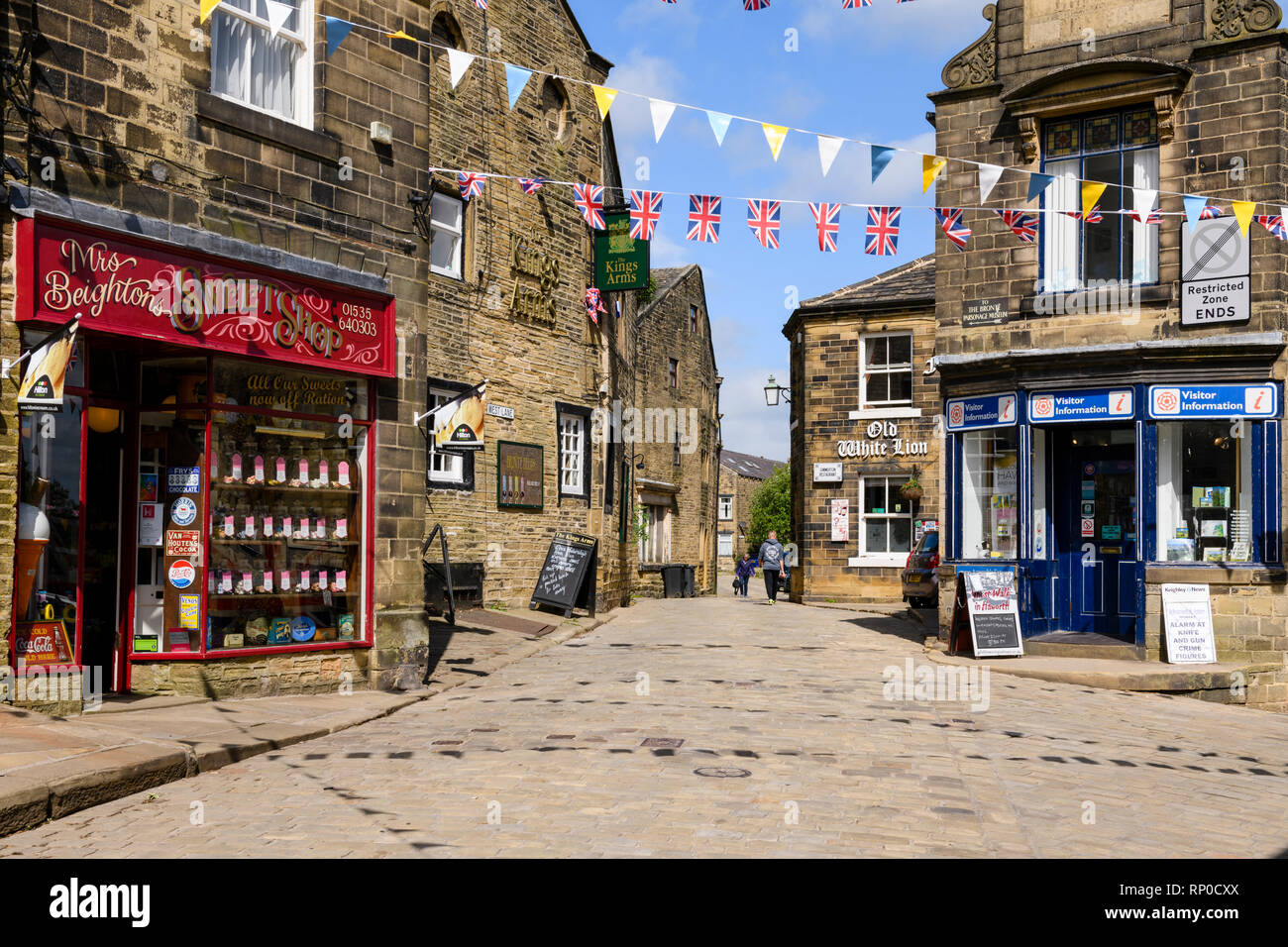 Traditionelle Sweet Shop, historische Gasthäuser, touristische Informationen & Bunting über gepflasterten Straße - Hauptstraße, Haworth Village, West Yorkshire, England, UK. Stockfoto