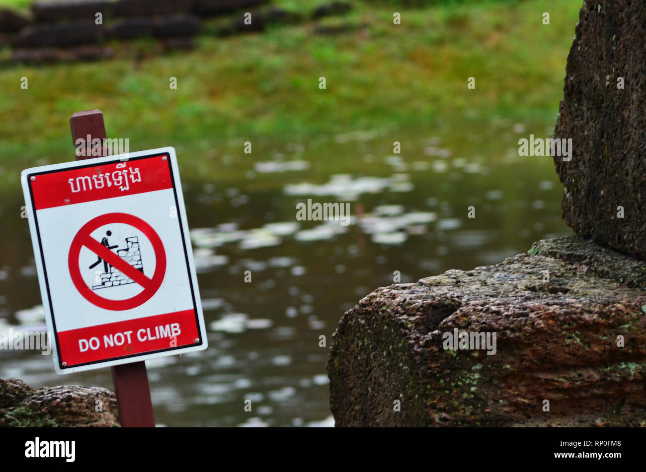 Steine neben einem Teich in einem zerstörten Wat in Kambodscha. Eine Warnung Schild, o nicht Klettern" mit einem Bild von jemand Klettern corssed ist neben dem da 'D Stockfoto