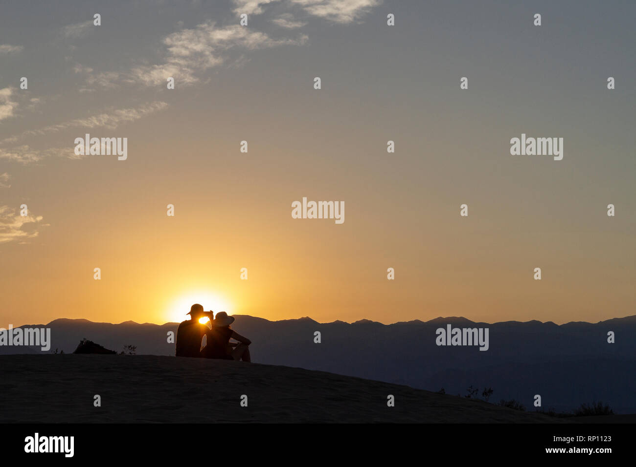Ein paar sitzt auf einer Düne bei Sonnenuntergang Silhouette gegen die Sonne, Mesquite flachen Sand Dünen, Death Valley National Park, California, United States Stockfoto