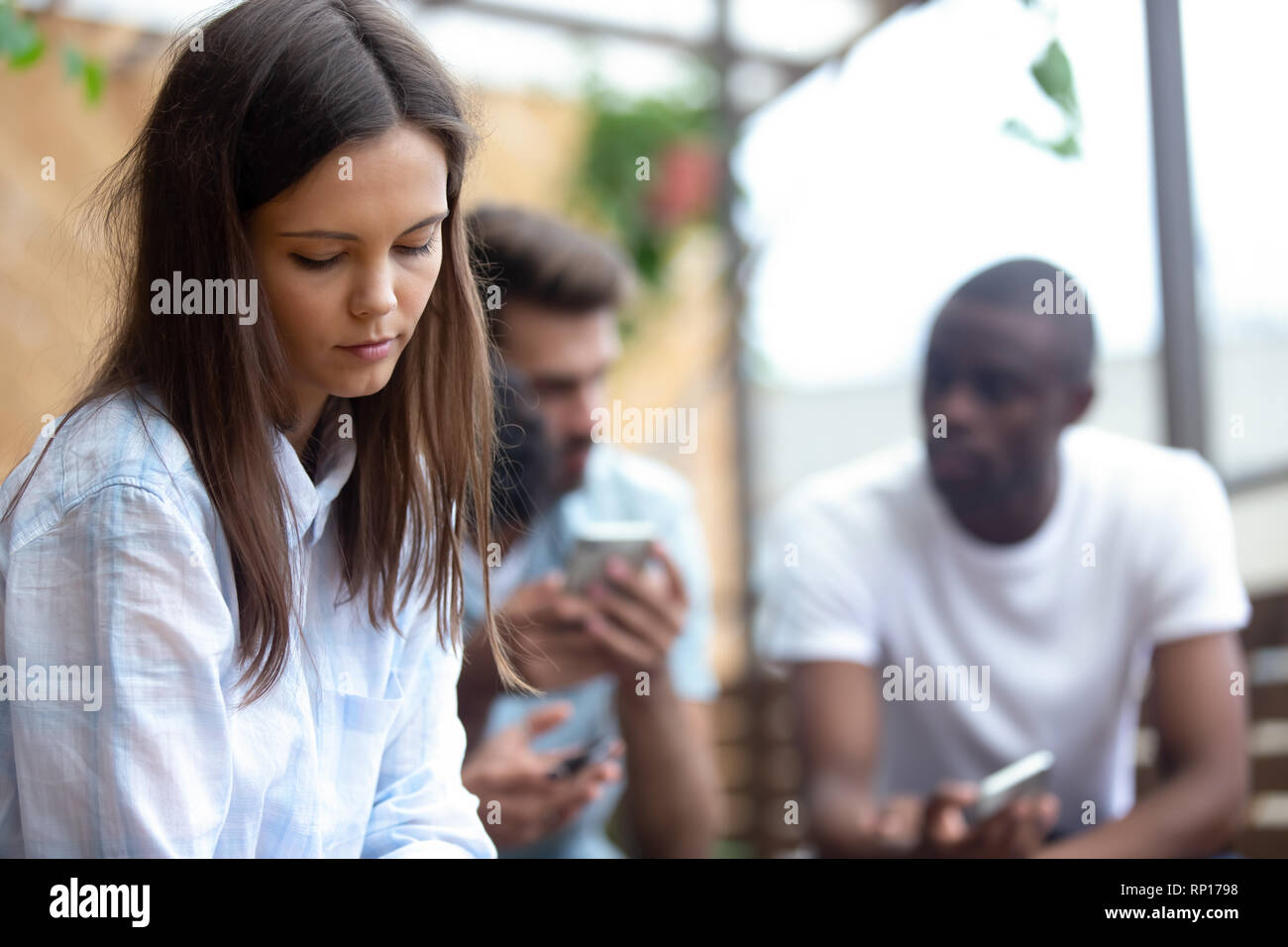 Traurige junge Frau alleine separat sitzen von Freunden Stockfoto