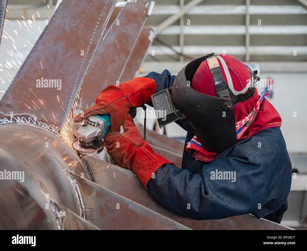Industrielle Arbeiter tragen eine Maske mit einem Winkelschleifer auf einer Stahlkonstruktion. Stockfoto