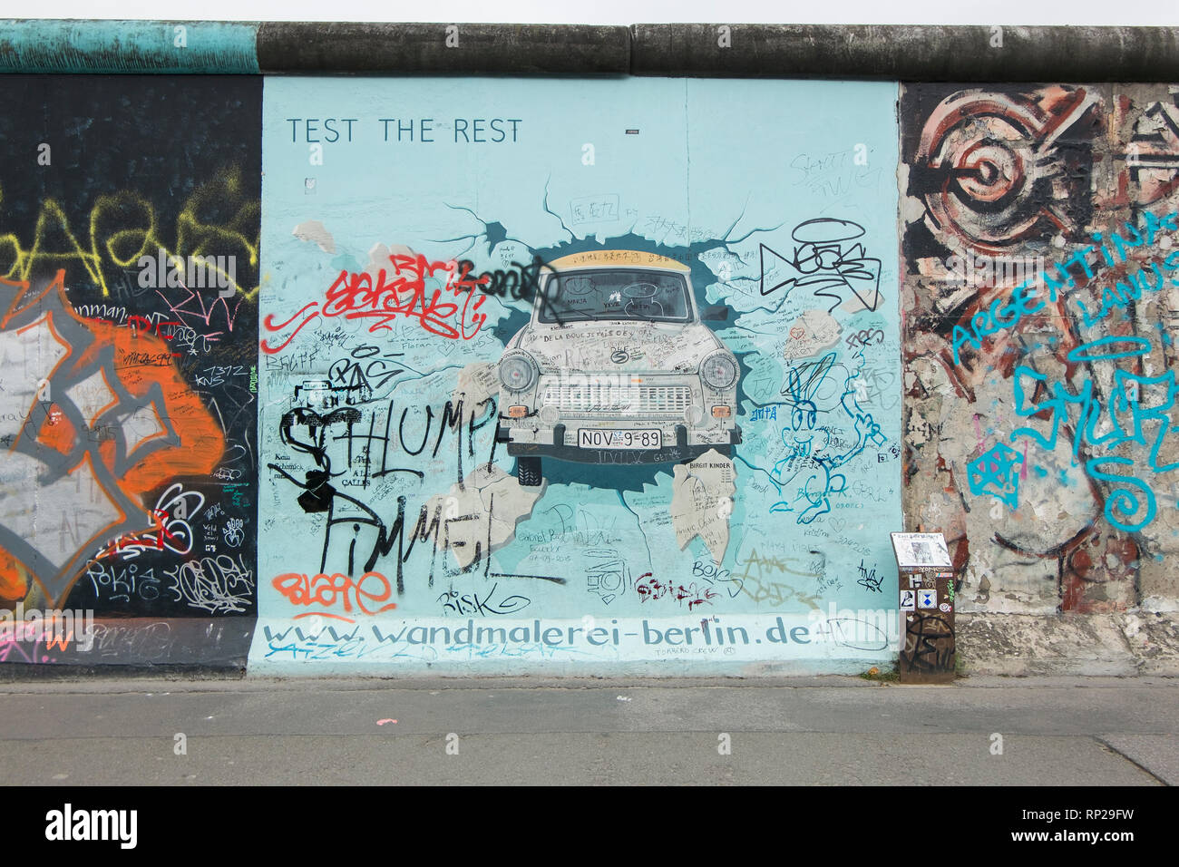 Die knarrenden Ostdeutschen auto Trabant macht ein Auftritt auf der Berliner Mauer in Berlin, Deutschland. Stockfoto