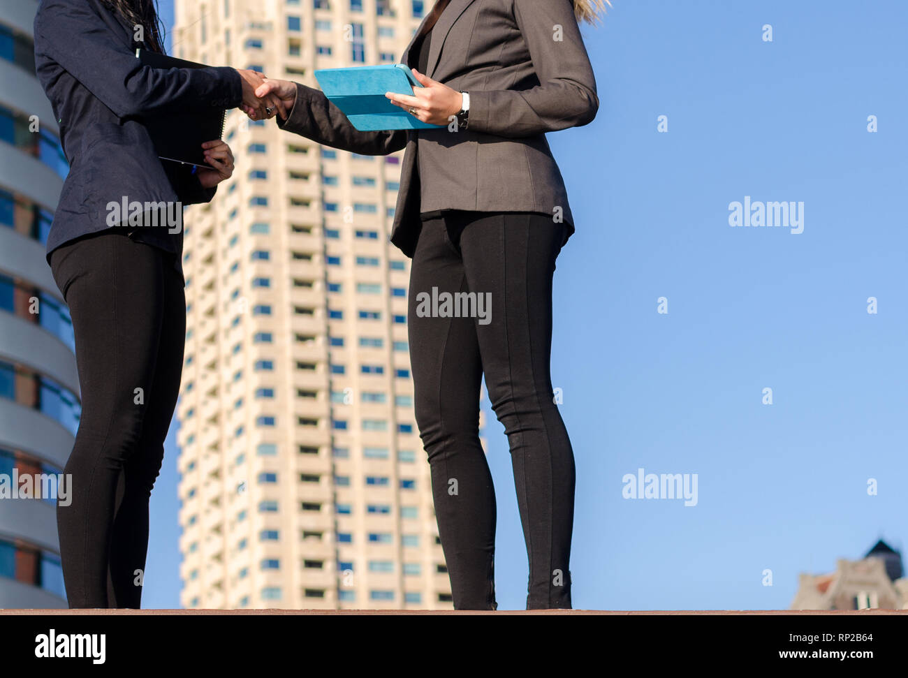Zwei unbekannte junge Frauen, die Tabletten Hände mit Wohnbauten im Hintergrund vorschlagen Immobilien oder Immobilientransaktion schütteln - Stockfoto