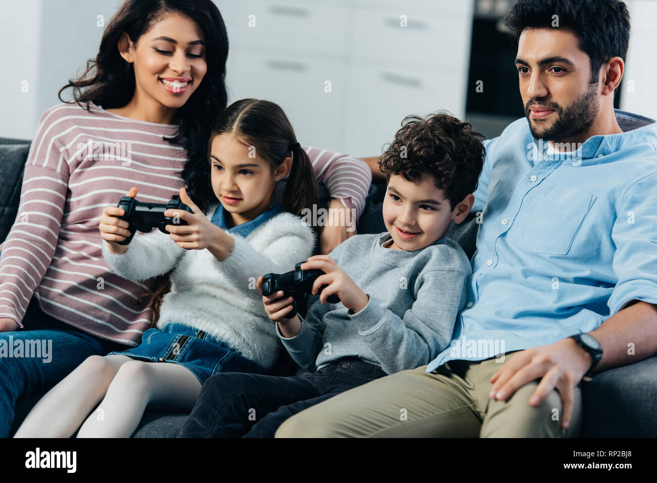 Fröhliche Eltern auf dem Sofa in der Nähe von spielenden Kinder video Spiel zu Hause sitzen Stockfoto