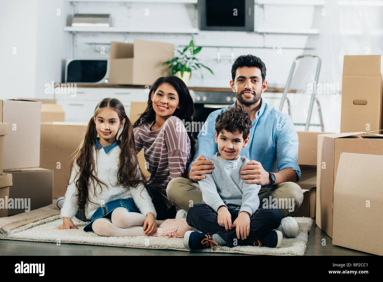 Latin, Mann und Frau in Teppich mit niedlichen Kinder im neuen Zuhause sitzen Stockfoto