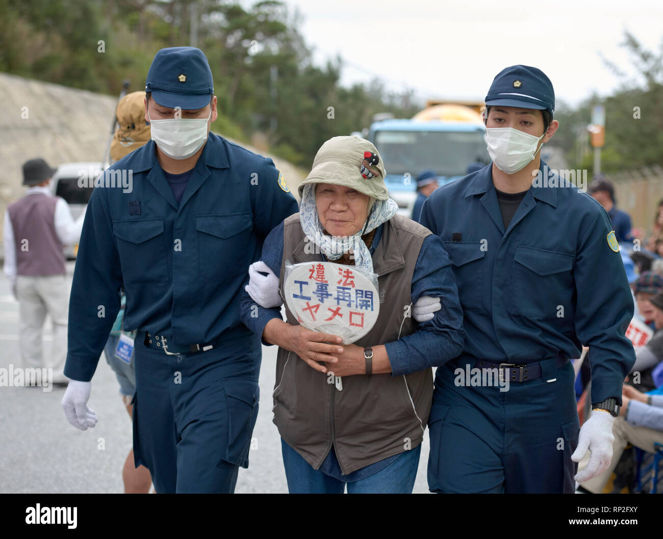 Henoko, Okinawa, Japan. 19 Feb, 2019. Die Polizei eine Frau weg vom Tor der Eine neue US Marine Corps Airbase in Henoko auf der japanischen Insel Okinawa konstruiert werden Escort. Dutzende Demonstranten, die wollen den Bau gestoppt, hatte physisch um für Lkw von der Basis, die Füllung in einem großen Teil des Meeresbodens ist um einen neuen Flugplatz zu bauen eingeben, das entfernt werden soll. Credit: Paul Jeffrey/Alamy leben Nachrichten Stockfoto