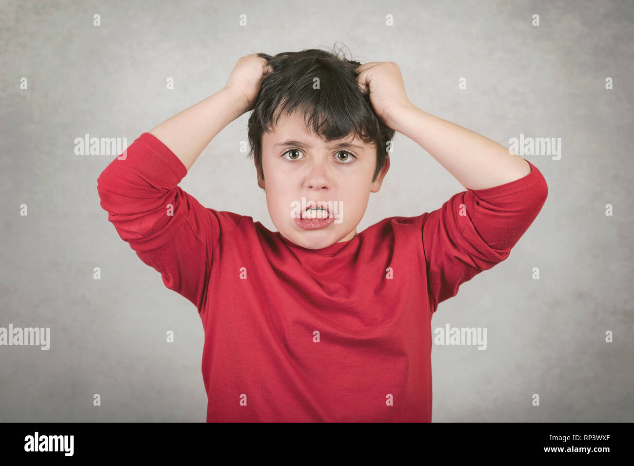 Wütenden Jungen, der seine Haare vor grauem Hintergrund zieht Stockfoto