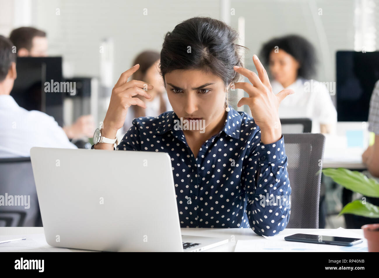 Verärgert indische weibliche Mitarbeiter am Schreibtisch im Büro, am PC-Bildschirm fühlt sich unglücklich und schockiert. Tausendjährige Hindu woman reading unangenehme notific Stockfoto