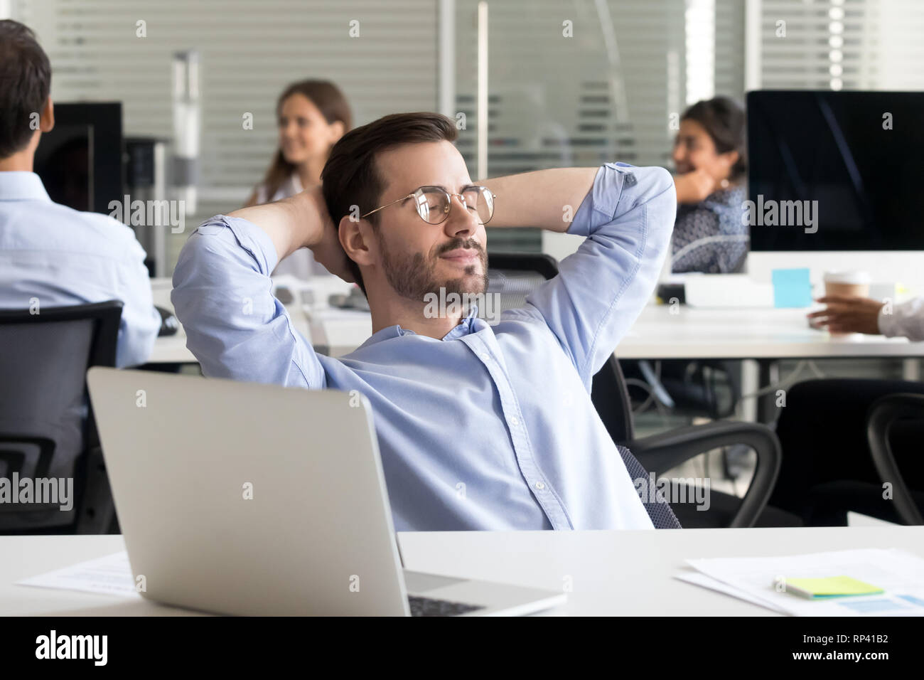 Büroangestellter mit geschlossenen Augen entspannt sitzen am Schreibtisch in Coworking Space cogitating hält die Hände hinter den Kopf. Mitarbeiter fertigen Arbeit ruhen Planung Stockfoto