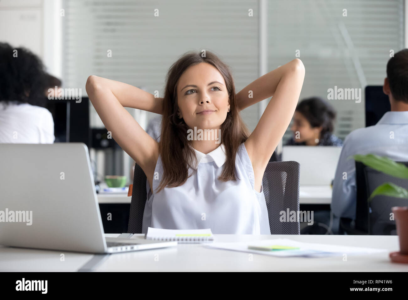 Tausendjährige nachdenklich positive Frau am Schreibtisch sitzen in Coworking Space fertige Arbeit hält die Hände hinter dem Kopf fühlt sich gut. Büro eine Pause d Stockfoto