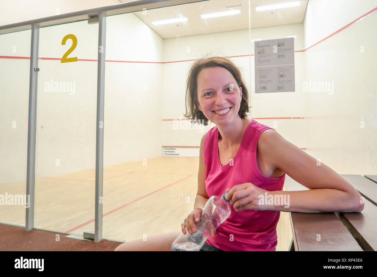 Eine Frau nimmt einen Bruch von Squash und trinkt aus der Flasche Wasser zur Erfrischung. Sie lächelt in die Kamera Stockfoto