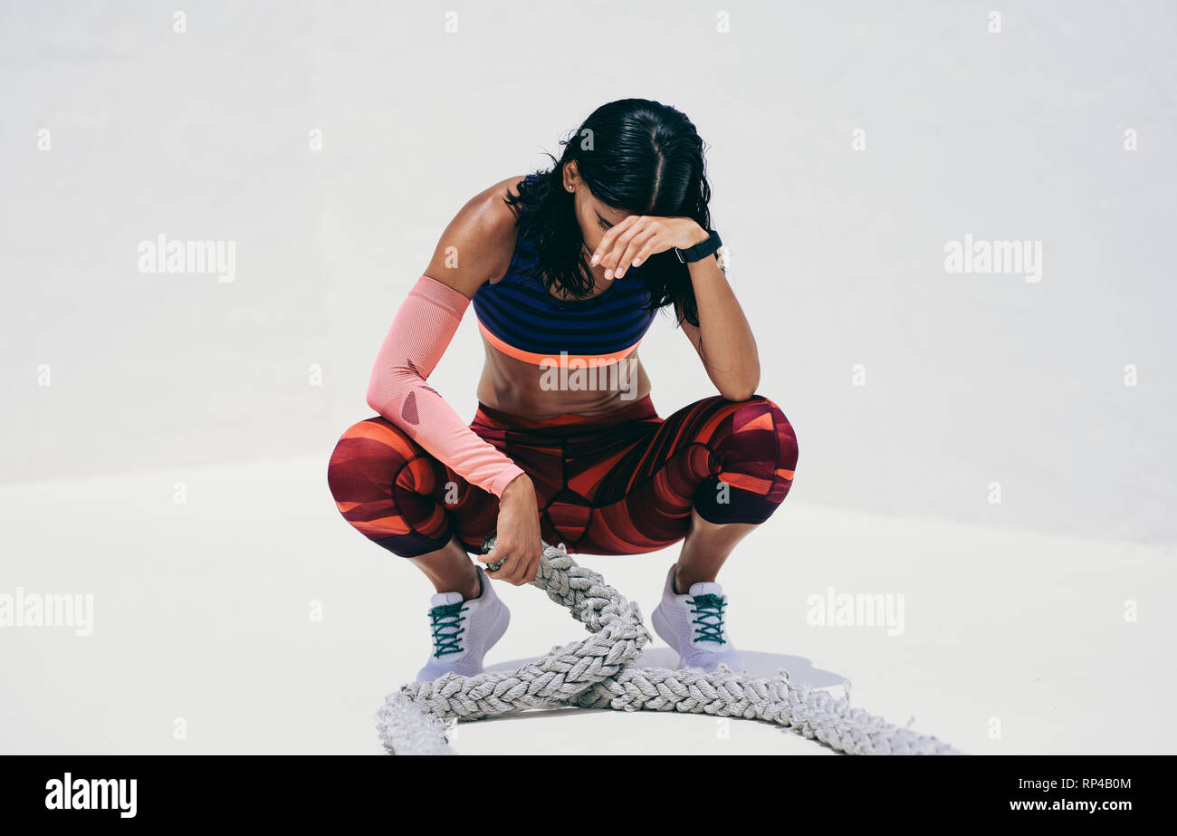 Fitness-Frau, die sich ausruht, auf ihren Zehen sitzend und Kampfseile hält. Frau in Fitnesskleidung, die eine Pause macht und sich nach einem harten Workout entspannt. Stockfoto