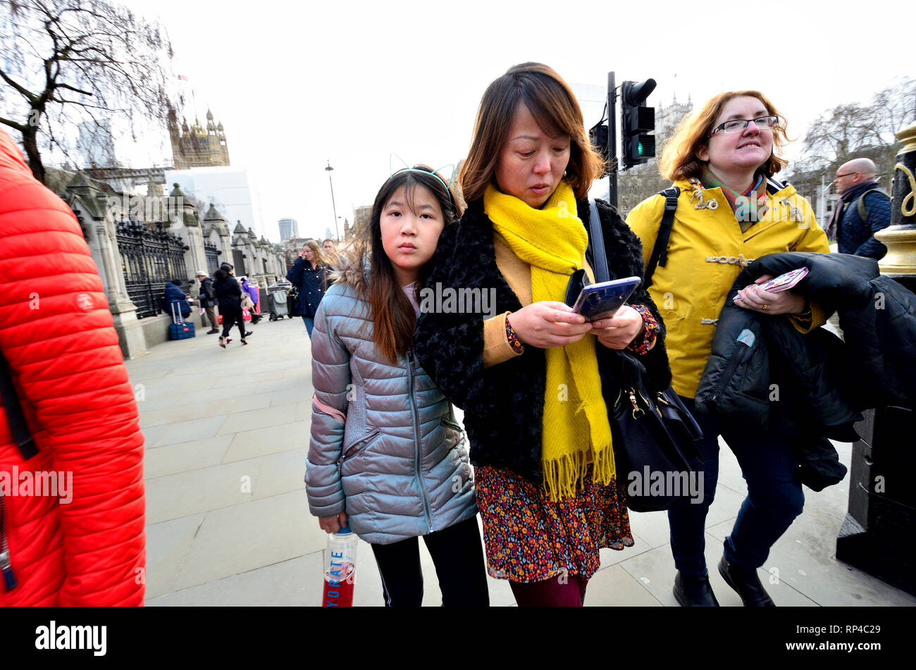 London, England, UK. Asiatische Mutter und Tochter zu Fuß auf der Straße - die Mutter an ihr Mobiltelefon suchen, Parliament Square Stockfoto