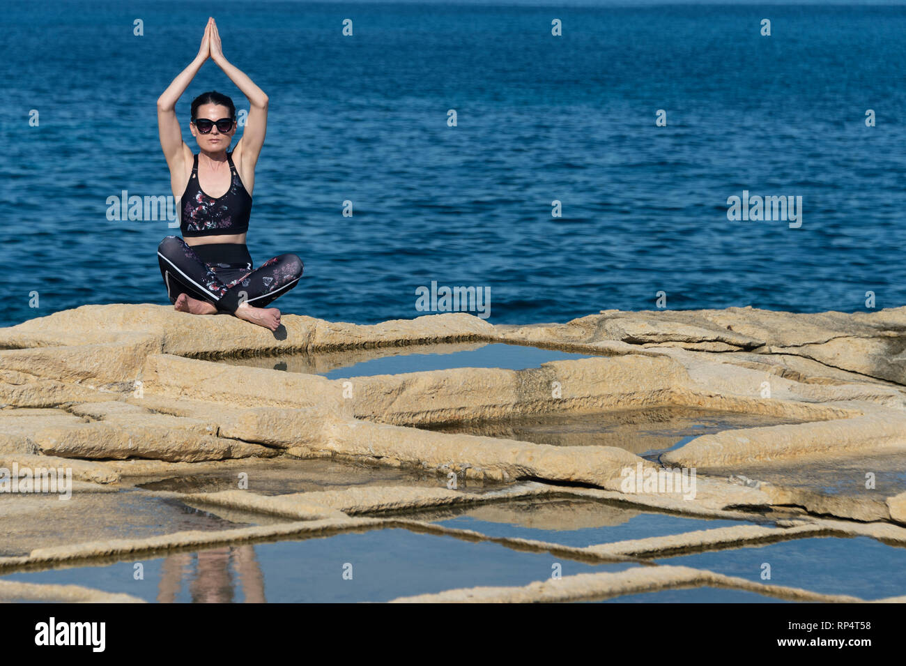 Frau auf dem Kalkstein Salinen in Malta sitzen, Yoga und Meditation in der Sonne Stockfoto