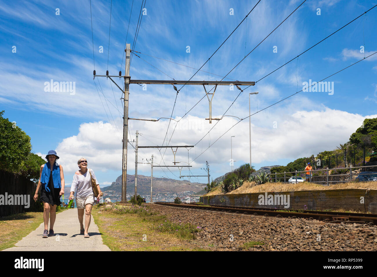 Küstenweg parallel zu einer Bahnlinie und zwei kaukasischen Frauen zu Fuß auf einem sonnigen Tag Sommer in Muizenberg, Kap, Südafrika Stockfoto