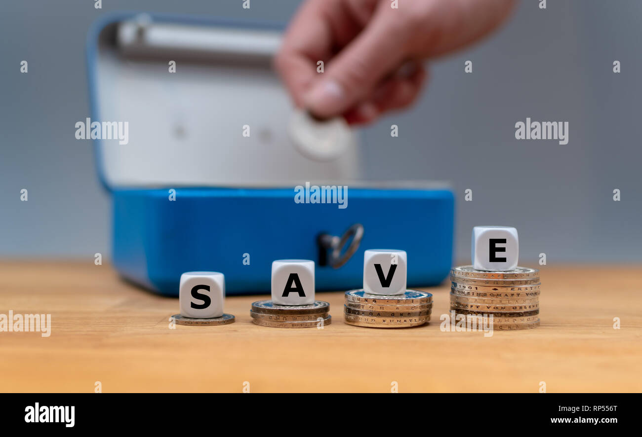 Würfel Form das Wort 'Save' an der Spitze der Stapel der Münzen. Im Hintergrund eine Hand eine Münze in der Kasse. Konzept der Geld sparen. Stockfoto