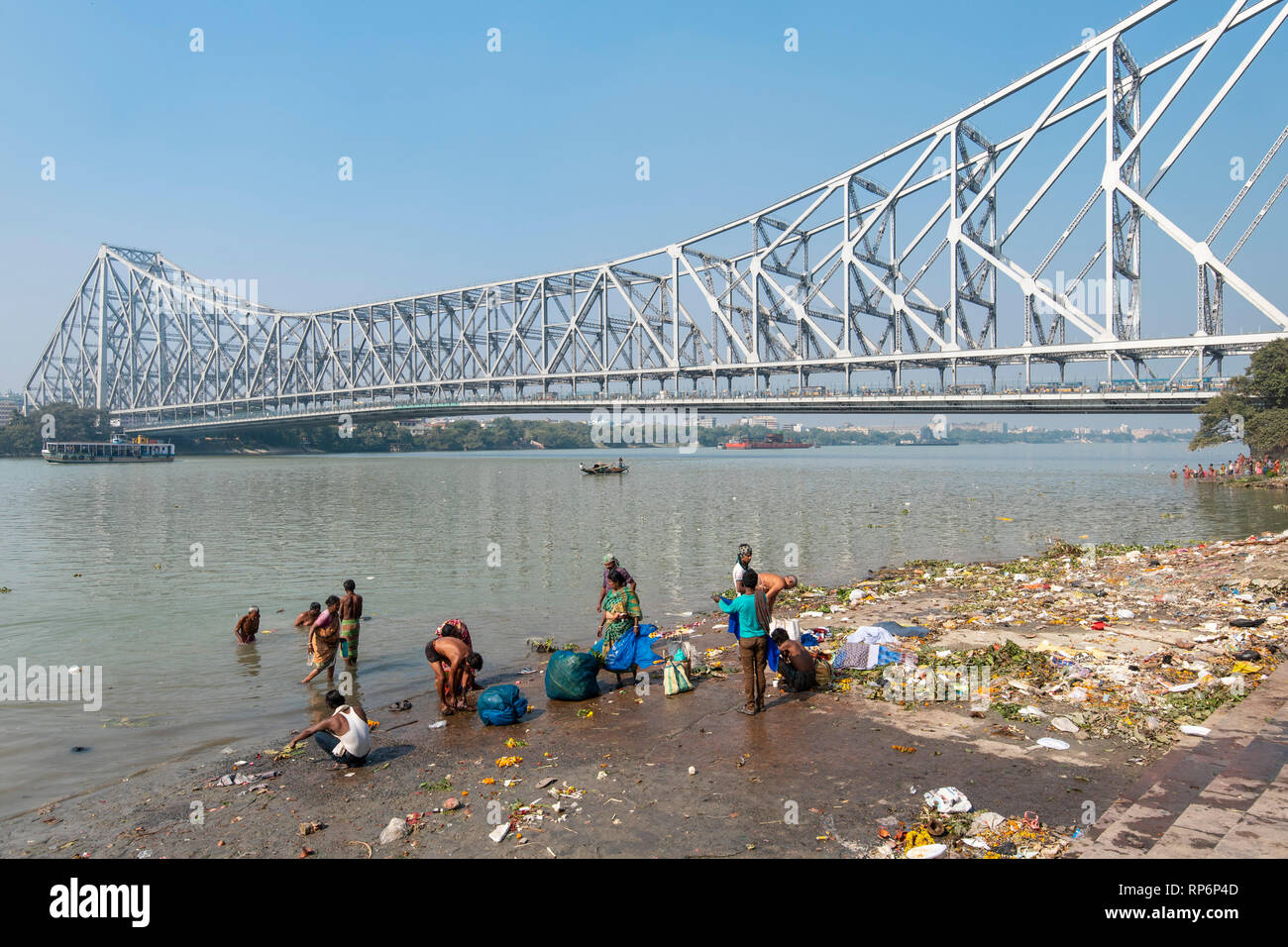 Howrah Bridge - im Volksmund bekannt als die Rabindra Setu mit Blick auf den Mullick Ghat mit Einheimischen baden Waschen an einem sonnigen Tag und blauer Himmel. Stockfoto