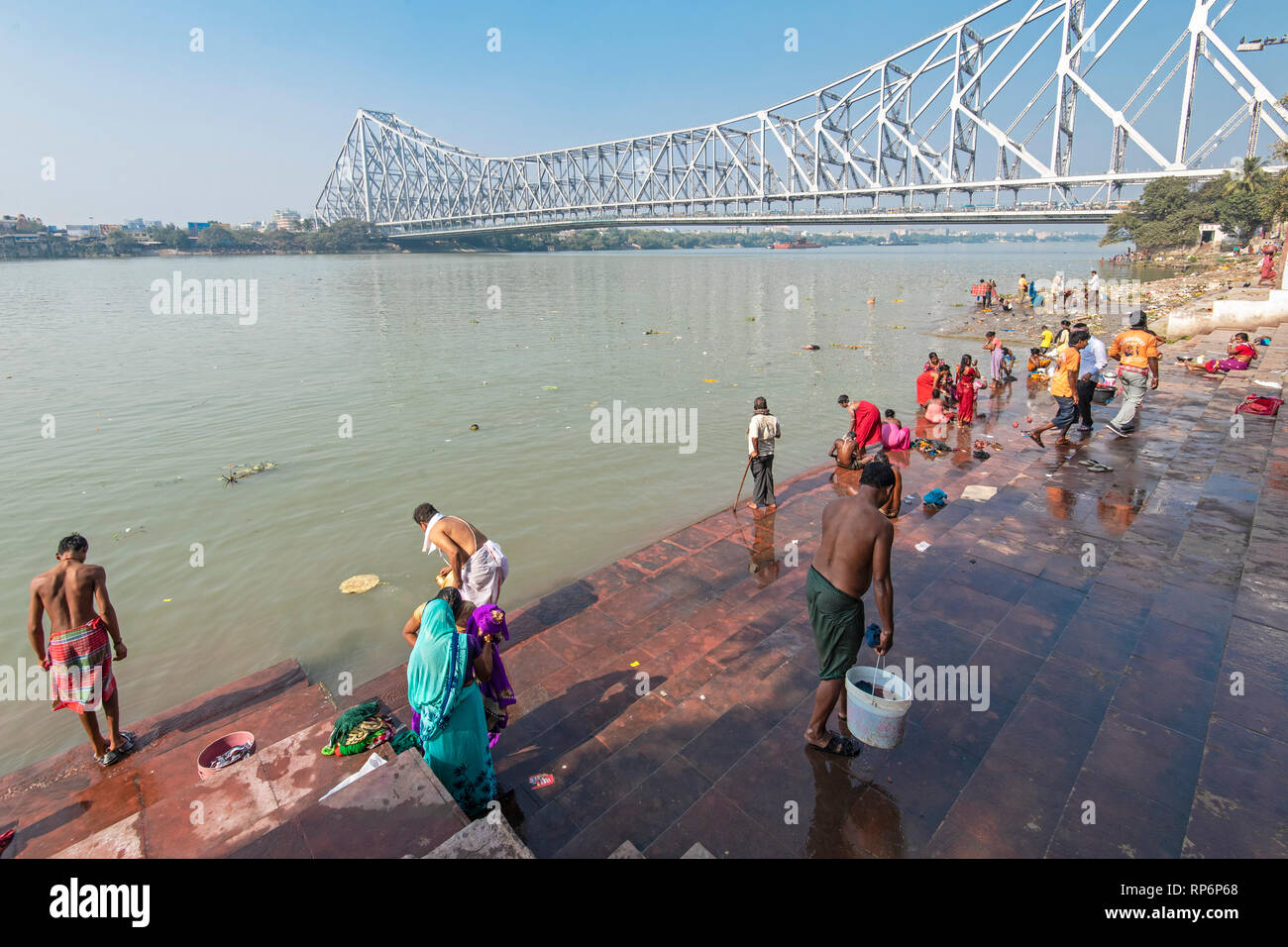 Howrah Bridge - im Volksmund bekannt als die Rabindra Setu mit Blick auf den Mullick Ghat mit Einheimischen baden Waschen an einem sonnigen Tag und blauer Himmel. Stockfoto