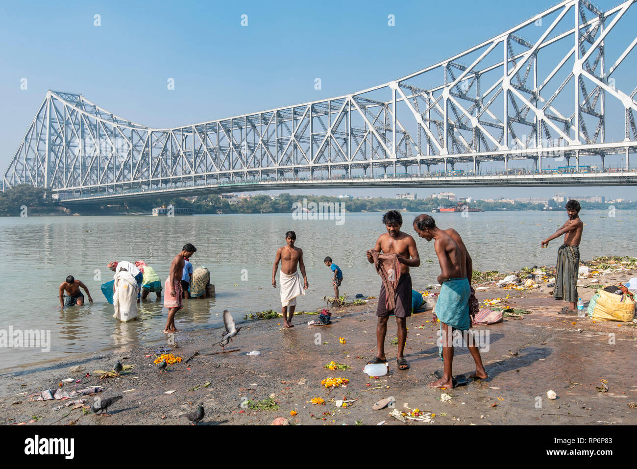 Howrah Bridge - im Volksmund bekannt als die Rabindra Setu mit Blick auf den Mullick Ghat mit Einheimischen baden Waschen an einem sonnigen Tag und blauer Himmel. Stockfoto
