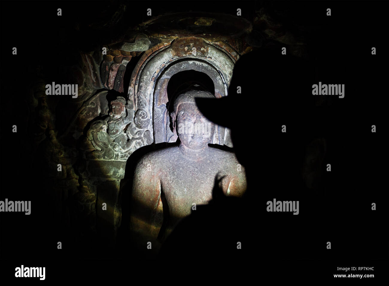Touristische Silhouette in Hut in der dunklen Höhle mit geschnitzten Statuen von Taschenlampe in Maharashtra, Indien Stockfoto